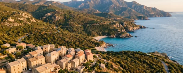 Vue aérienne d'une zone côtière corse montrant l'architecture traditionnelle en pierre avec toits de tuiles, le maquis méditerranéen et le relief vallonné caractéristique de l'île, sous une lumière dorée de fin de journée